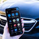 A photo of a hand holding up a Pixel 5 with the Assistant Driving Mode interface on it, with a car in the background